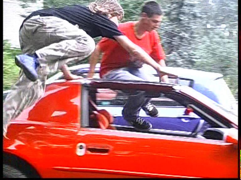 Zwei Darsteller bei einer bewegten Filmszene am roten Pontiac