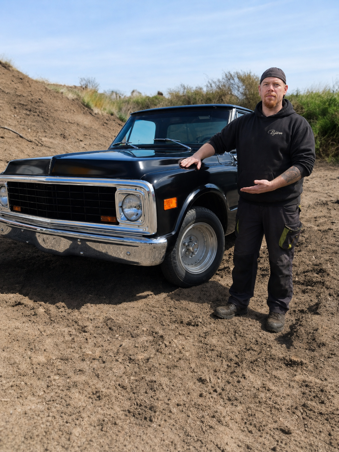 Björn Börner steht neben einem schwarzen klassischen Chevrolet Pickup und präsentiert das Fahrzeug